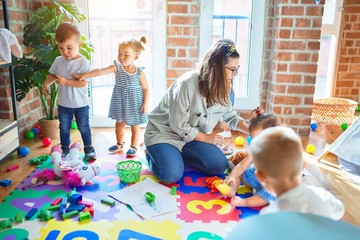 Beautiful teacher and group of toddlers playing around lots of toys at kindergarten