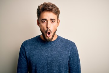 Young handsome man with beard wearing casual sweater standing over white background afraid and shocked with surprise expression, fear and excited face.