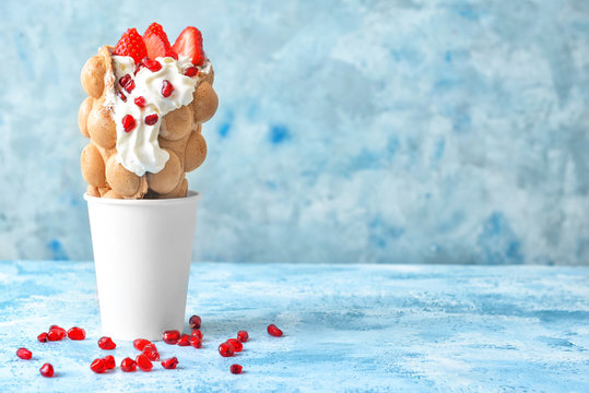 Cup with delicious sweet bubble waffle on color background