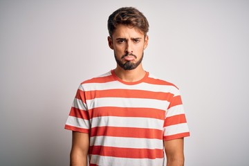 Obraz premium Young handsome man with beard wearing striped t-shirt standing over white background depressed and worry for distress, crying angry and afraid. Sad expression.