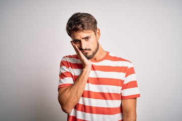 Young handsome man with beard wearing striped t-shirt standing over white background thinking looking tired and bored with depression problems with crossed arms.