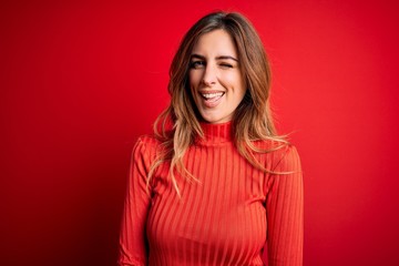 Fototapeta premium Young beautiful brunette woman wearing casual turtleneck sweater over red background winking looking at the camera with sexy expression, cheerful and happy face.