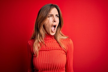 Young beautiful brunette woman wearing casual turtleneck sweater over red background angry and mad...
