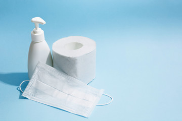 Antiseptic sanitizer gel, medicine face mask and toilet paper roll on blue background