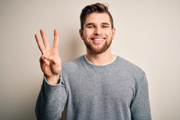 Young handsome blond man with beard and blue eyes wearing casual sweater showing and pointing up with fingers number three while smiling confident and happy.