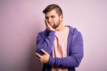 Young blond man with beard and blue eyes wearing purple sweatshirt over pink background thinking looking tired and bored with depression problems with crossed arms.