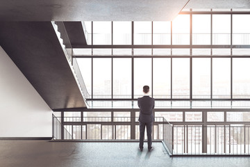 Businessman looking on big window in modern high-rise building interior.