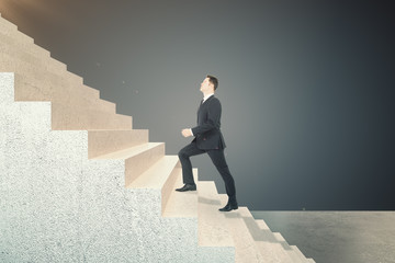 Side view of young businessman climbing on abstract stairs.