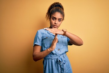 Young beautiful african american girl wearing denim dress standing over yellow background Doing...