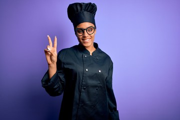 Young african american chef girl wearing cooker uniform and hat over purple background smiling looking to the camera showing fingers doing victory sign. Number two.