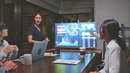 Young Asian businesswoman lead group of business financial team in strategic meeting presentation, work late night in office. Marketing strategy analysis, stock market trading, or corporate teamwork - Powered by Adobe