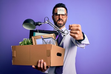 Young handsome businessman with beard holding cardboard box with fired reminder on head annoyed and frustrated shouting with anger, crazy and yelling with raised hand, anger concept
