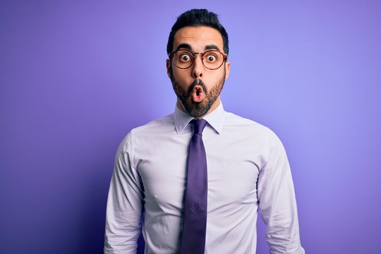 Handsome businessman with beard wearing casual tie and glasses over purple background afraid and shocked with surprise expression, fear and excited face.