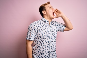 Young handsome redhead man wearing casual summer shirt standing over pink background shouting and screaming loud to side with hand on mouth. Communication concept.