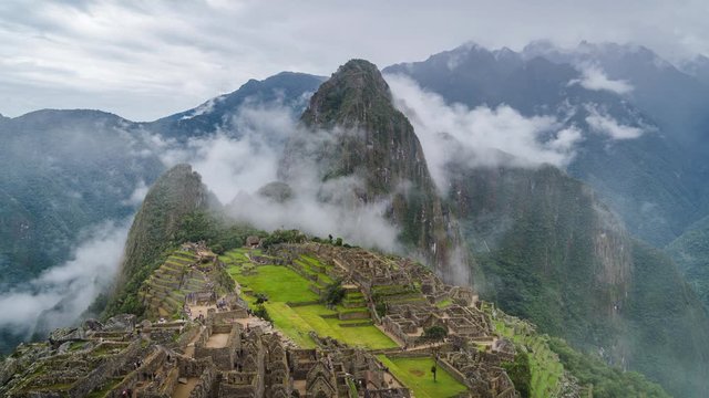 Zoom out time lapse view of mysterious Inca ruins of Machu Picchu shrouded in mist high in the Andes mountain range, Cusco Region, Peru.