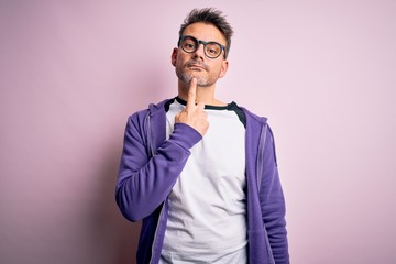Young handsome man wearing purple sweatshirt and glasses standing over pink background Thinking...