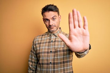 Fototapeta premium Young handsome man wearing casual shirt standing over isolated yellow background doing stop sing with palm of the hand. Warning expression with negative and serious gesture on the face.