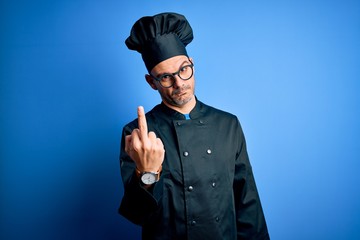 Young handsome chef man wearing cooker uniform and hat over isolated blue background Showing middle...