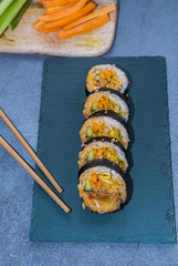 Kimbap roll with pork, cucumber, carrot and radish on a slate place with chopsticks. Korean cuisine. Vertical picture.