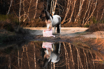 junge Frau kniet vor ihrem Pony an einem See mit einer Spiegelung
