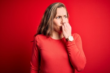 Young beautiful blonde woman wearing casual t-shirt standing over isolated red background looking stressed and nervous with hands on mouth biting nails. Anxiety problem.