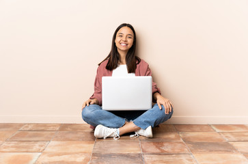 Young mixed race woman with a laptop sitting on the floor laughing