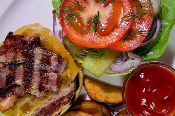 Burger with fried bacon, french fries, vegetables and ketchup on a white plate.View from above.Close-up.Binge eating