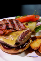 Close-up of Burger with fried bacon, french fries, vegetables and ketchup on a white plate.Unhealthy food
