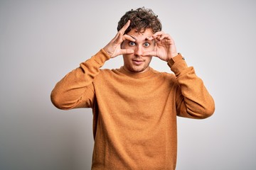 Young blond handsome man with curly hair wearing casual sweater over white background Trying to open eyes with fingers, sleepy and tired for morning fatigue