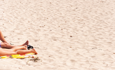 Legs of a couple sunbathing on a lonely sandy beach