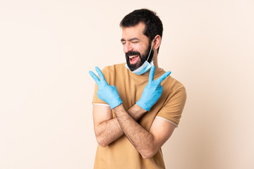 Caucasian man with beard protecting from the coronavirus with a mask and gloves over isolated background smiling and showing victory sign