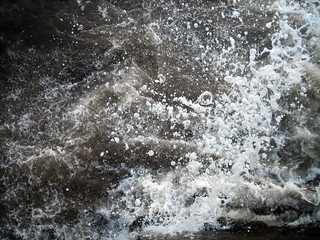 Naklejka na ściany i meble Sea waves of dark water beat against the coastal rocks. An infinite number of splashes, drops of water and white foam are scattered.