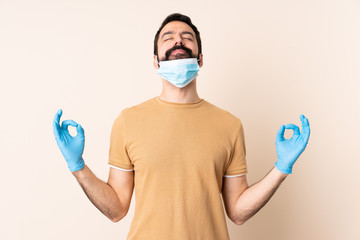 Caucasian man with beard protecting from the coronavirus with a mask and gloves over isolated background in zen pose