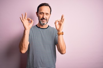 Middle age hoary man wearing casual striped t-shirt standing over isolated pink background relax and smiling with eyes closed doing meditation gesture with fingers. Yoga concept.