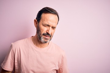 Middle age hoary man wearing casual t-shirt standing over isolated pink background with hand on stomach because indigestion, painful illness feeling unwell. Ache concept.