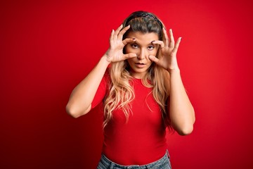 Young beautiful blonde woman wearing casual t-shirt standing over isolated red background Trying to open eyes with fingers, sleepy and tired for morning fatigue