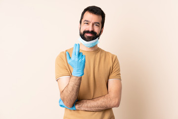 Caucasian man with beard protecting from the coronavirus with a mask and gloves over isolated background inviting to come with hand. Happy that you came