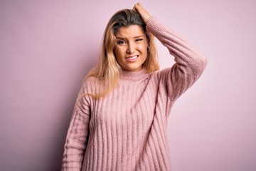 Young beautiful blonde woman wearing casual pink sweater over isolated background confuse and wonder about question. Uncertain with doubt, thinking with hand on head. Pensive concept.