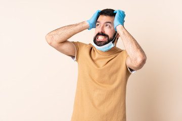 Fototapeta premium Caucasian man with beard protecting from the coronavirus with a mask and gloves over isolated background stressed overwhelmed