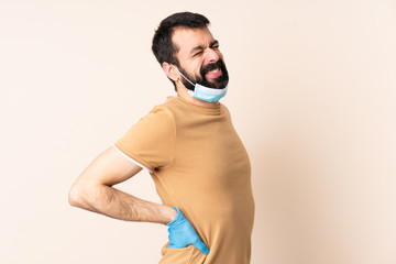 Caucasian man with beard protecting from the coronavirus with a mask and gloves over isolated background suffering from backache for having made an effort