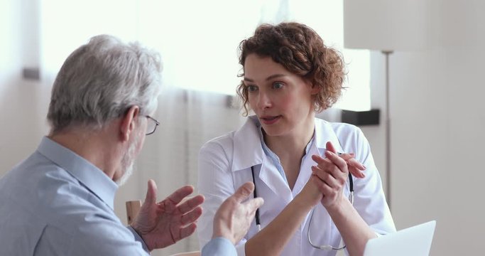 Female physician explaining medicine prescription to ill sick senior adult client at medical visit. Young doctor consulting examining old man patient in hospital. Elderly person health care concept