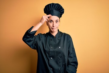 Young beautiful chef woman wearing cooker uniform and hat standing over yellow background worried and stressed about a problem with hand on forehead, nervous and anxious for crisis
