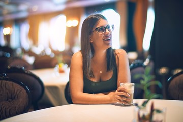 Young beautiful woman smiling happy and confident. Sitting with smile on face holding glass of coffee at restaurant