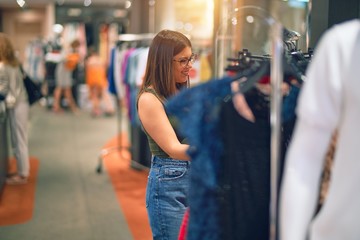 Young beautiful woman smiling happy and confident. Standing with smile on face looking clothes at store