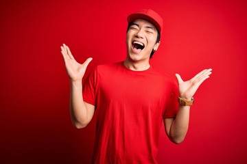 Young handsome chinese delivery man wearing cap standing over isolated red background celebrating...