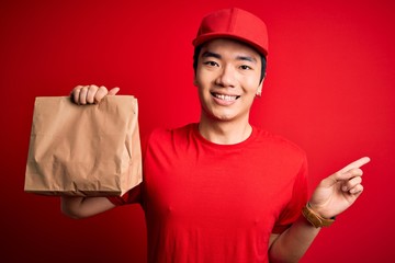Young handsome chinese delivery man holding takeaway paper bag with food very happy pointing with hand and finger to the side