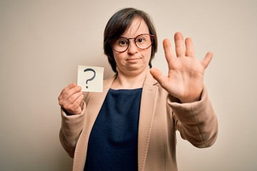 Young down syndrome business woman holding question mark paper as doubt symbol with open hand doing stop sign with serious and confident expression, defense gesture