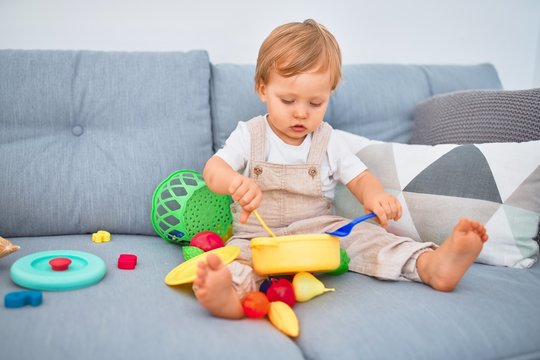 Adorable blonde toddler sitting on the sofa playing with plastic meals toys at home