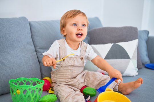 Adorable blonde toddler smiling happy sitting on the sofa playing with plastic meals toys at home