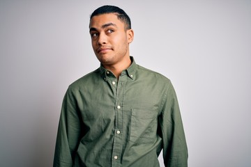 Young brazilian man wearing casual shirt standing over isolated white background smiling looking to the side and staring away thinking.